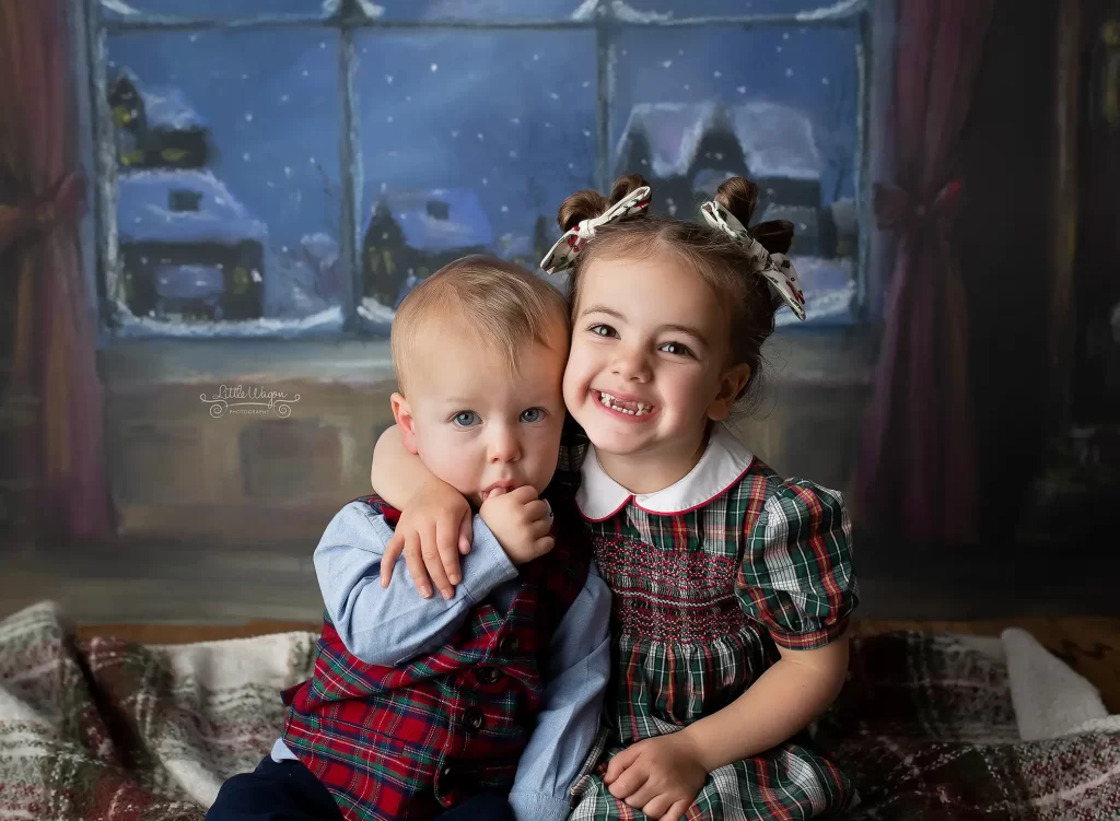 Two adorable siblings taking their photos at Little Wagon Photography during a Christmas photo session.